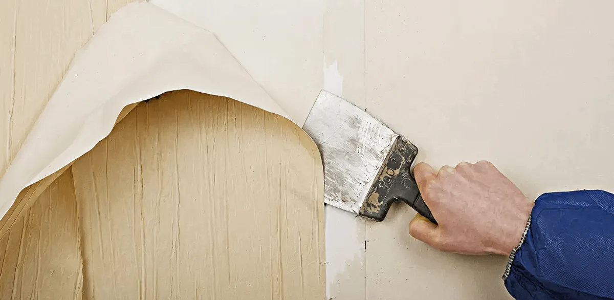Handyman removing wallpaper with a scraper for wall preparation in Cambridge, MA