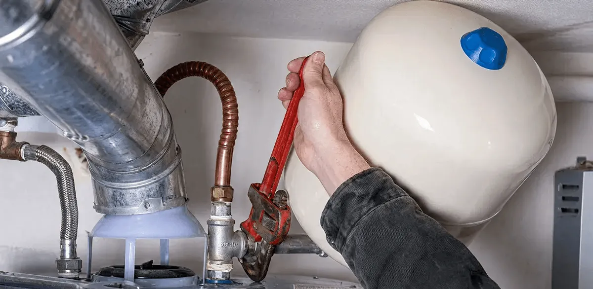 Water heater repair technician tightening plumbing connections near a tank unit in Cambridge, MA